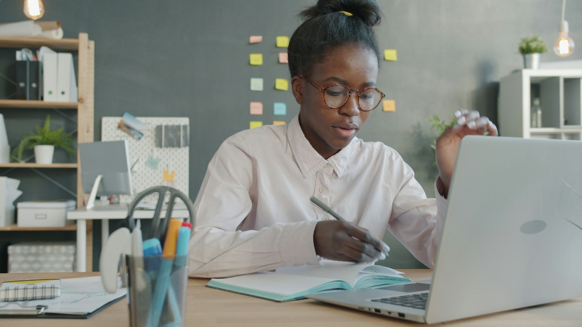 Woman working at a desk with laptop and notebook.